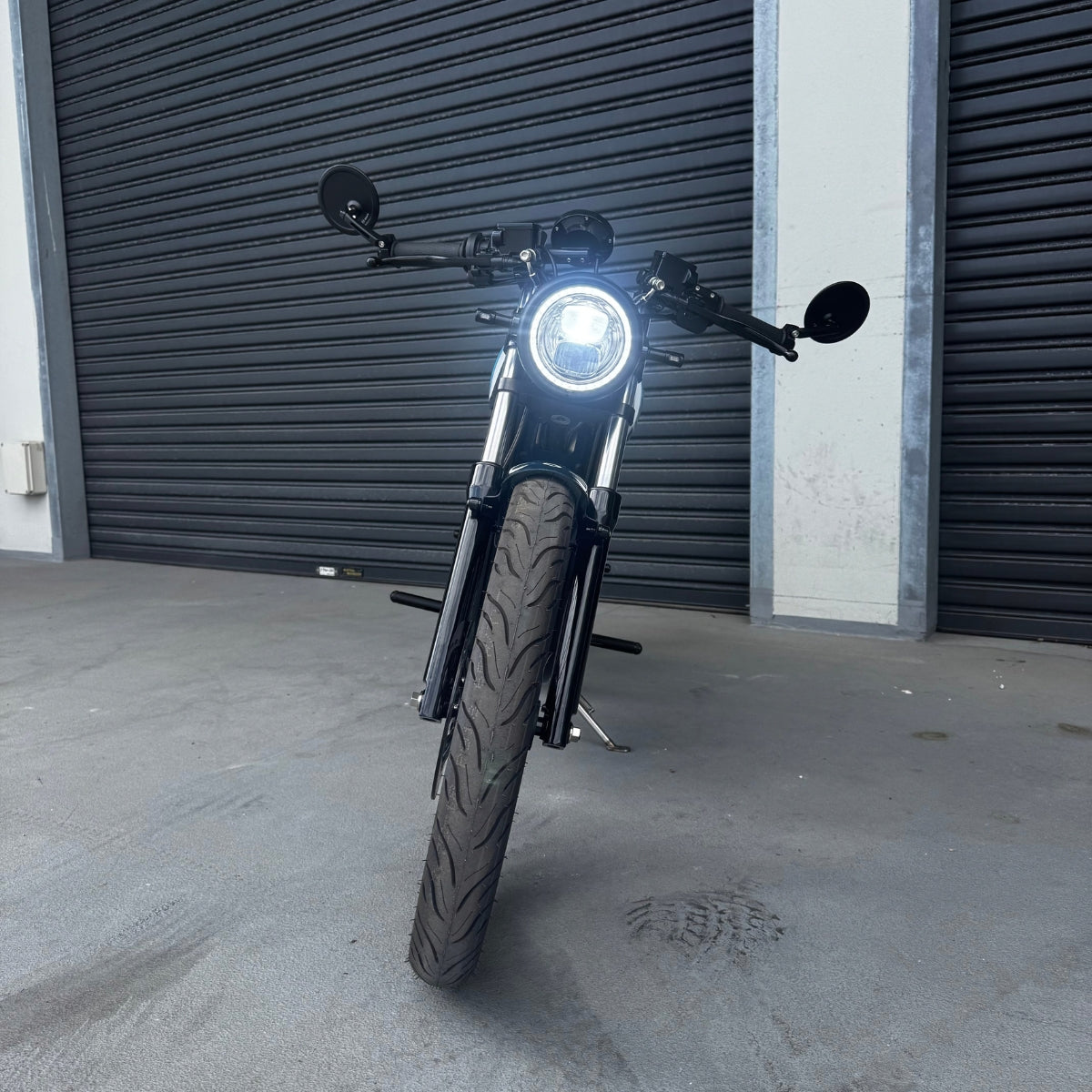 A limited edition phantom Streetdog electric motorcycle parked in front of a garage roller door. The tank and side panels are dark blue with light blue and white accents.