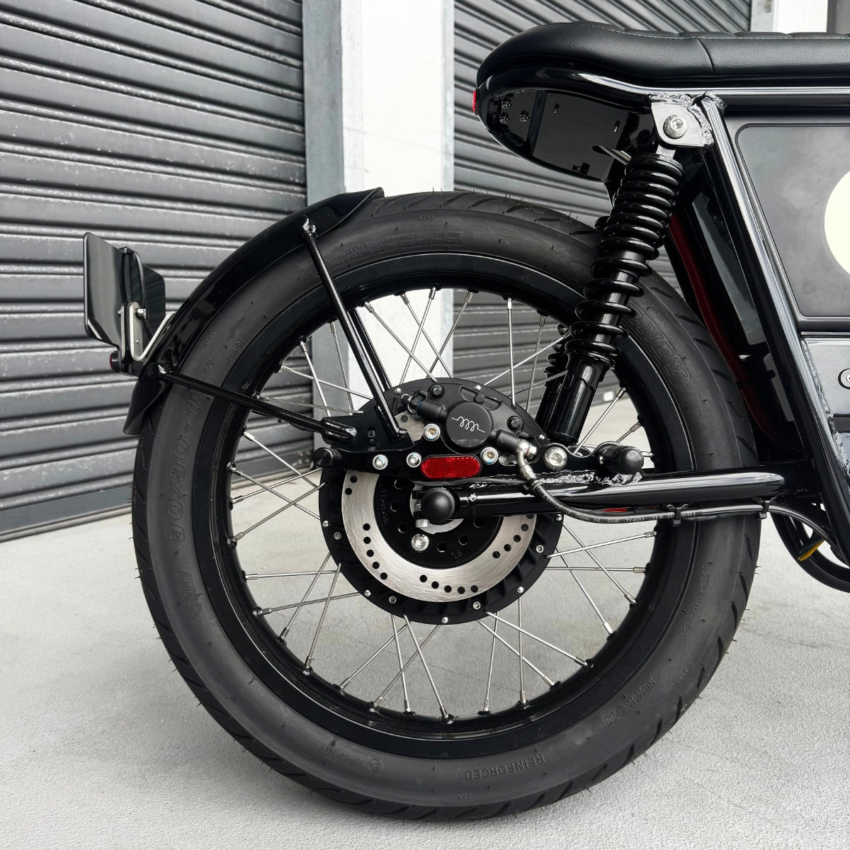 A Streetdog electric motorcycle parked in front of a garage roller door. The tank and side panels are baby blue and feature a cream stripe.