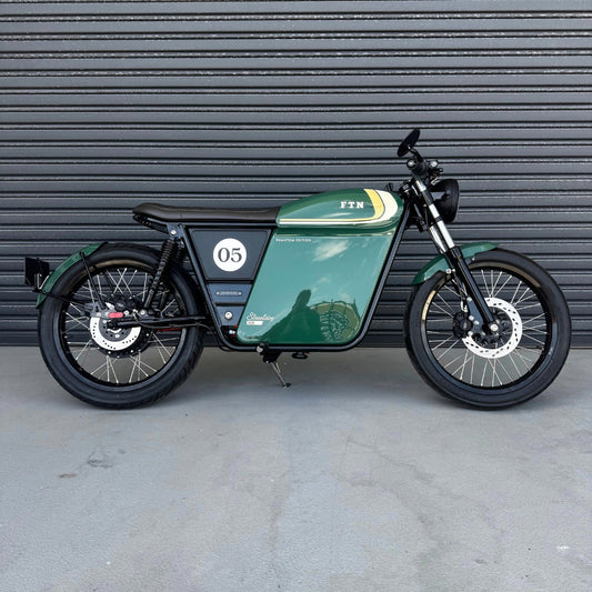 A limited edition phantom Streetdog electric motorcycle parked in front of a garage roller door. The tank and side panels are dark green with light cream and white accents.