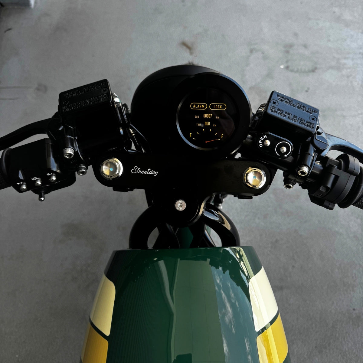 A limited edition phantom Streetdog electric motorcycle parked in front of a garage roller door. The tank and side panels are dark green with light cream and white accents.