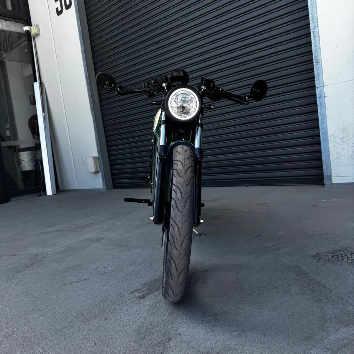A limited edition phantom Streetdog electric motorcycle parked in front of a garage roller door. The tank and side panels are dark green with light cream and white accents.
