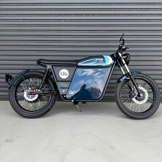 A limited edition phantom Streetdog electric motorcycle parked in front of a garage roller door. The tank and side panels are dark blue with light blue and white accents. 