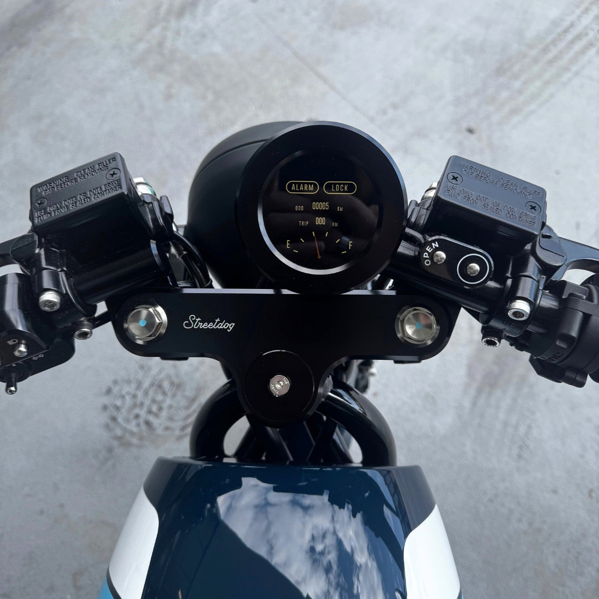 A limited edition phantom Streetdog electric motorcycle parked in front of a garage roller door. The tank and side panels are dark blue with light blue and white accents. 